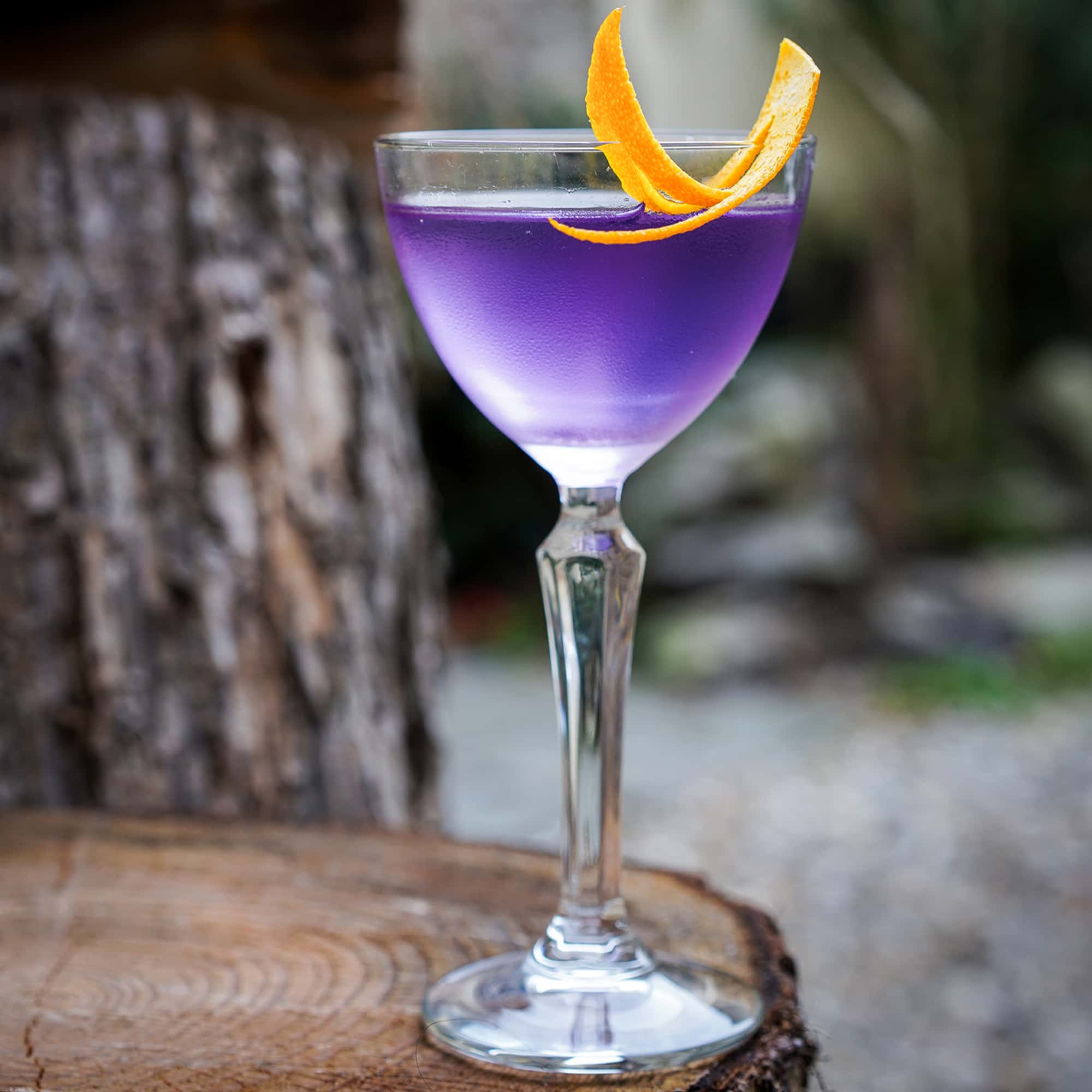 A cocktail with a lavendar hue and a citrus garnish.